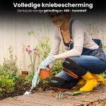 Vrouw in overall met gele laarzen en handschoenen, knielend in een tuin met de zwarte en oranje kniebeschermers.