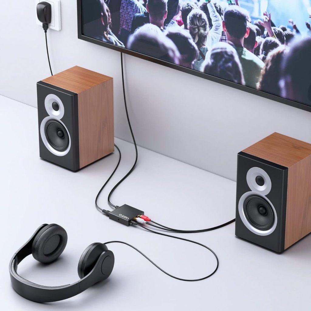 Zwarte Clerby audioconverter aangesloten tussen een TV, twee houten speakers en een koptelefoon.