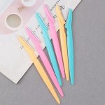 Zes gezichts-scheermesjes in pastelkleuren roze, turquoise en geel, op papier.